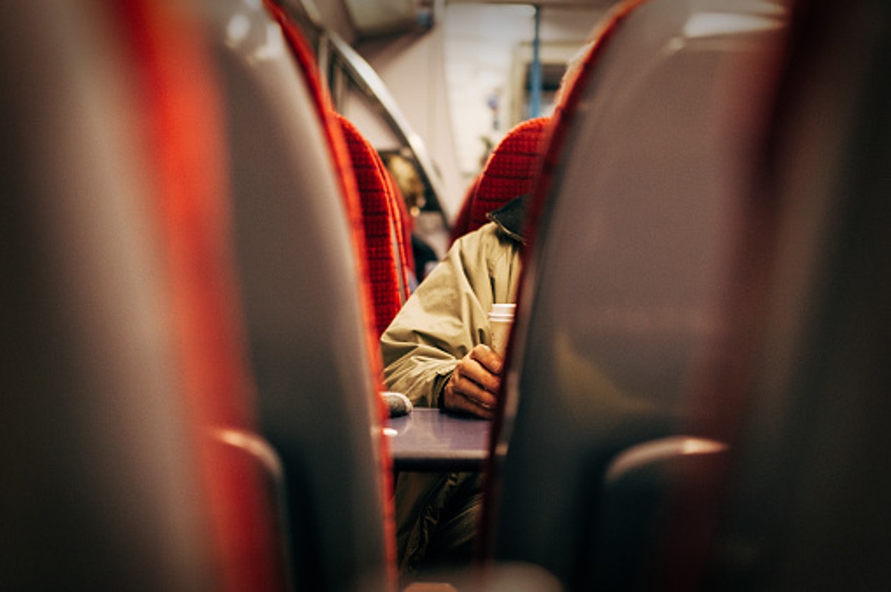 An image of a train. The picture has been taken between two trains seats and looking ahead into the four red seats in front.