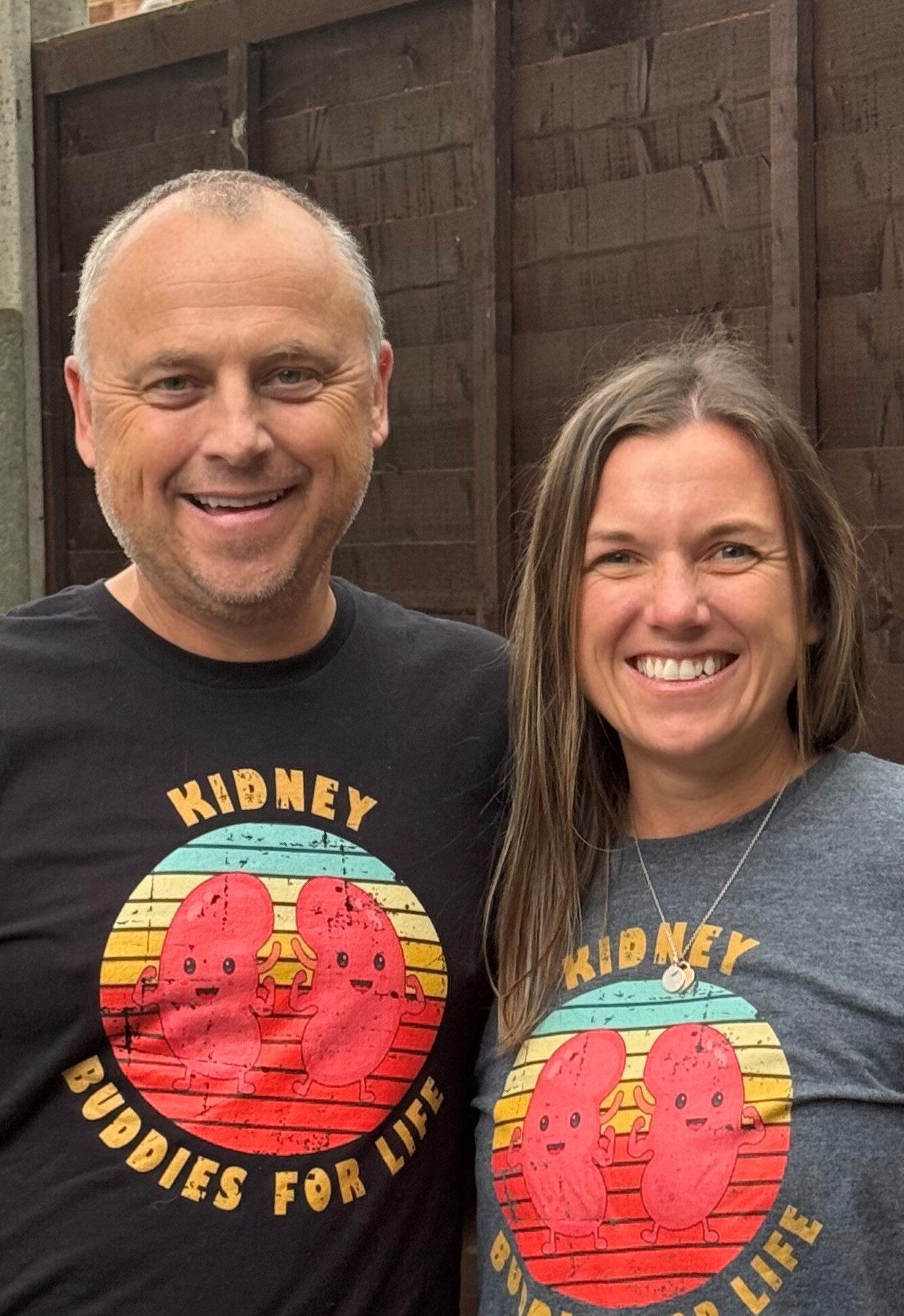 Living kidney recipient Andy standing beside his donor, Laura. They are both wearing the same top with a picture of two cartoon kidneys surrounded by the words 'kidney buddies for life'