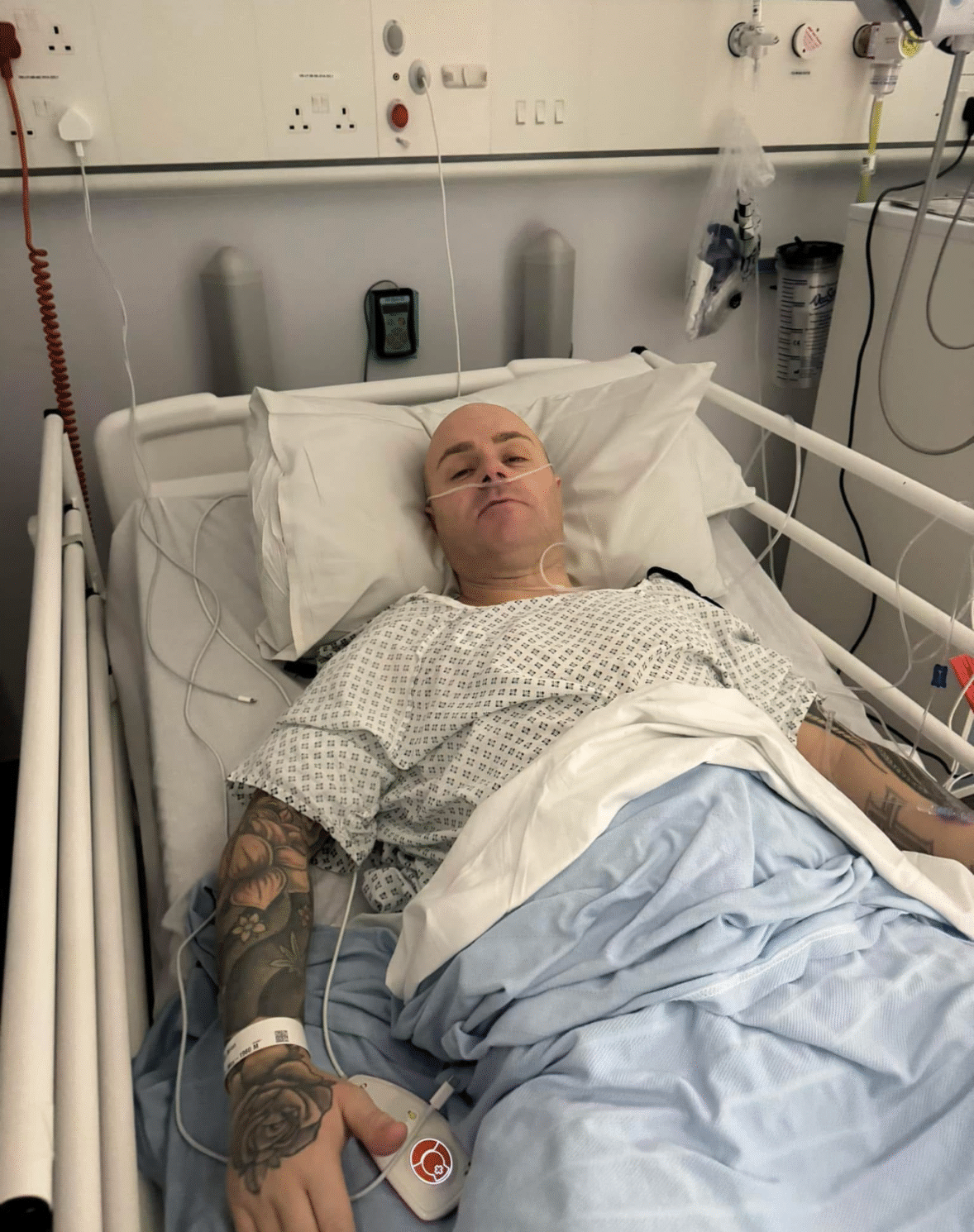 Image of living kidney donor Brian lying in a hospital bed dressed in a hospital gown. He looks relaxed, with his eyes barely open.