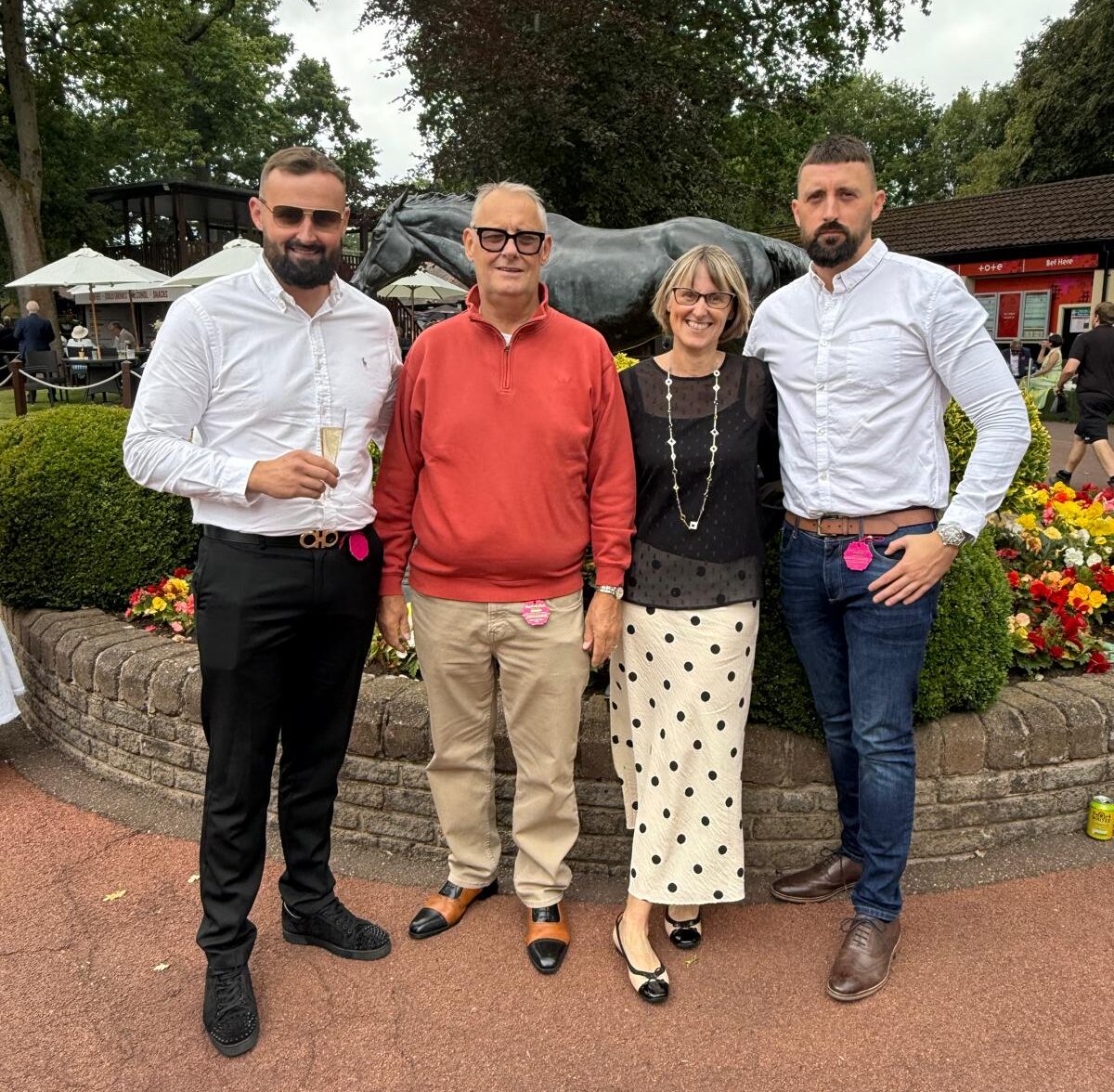 Living kidney recipient Mark posing for a photo alongside his two sons and his wife. They are all dressed in smart clothes and standing in front of a green space featuring bushes and flowers.