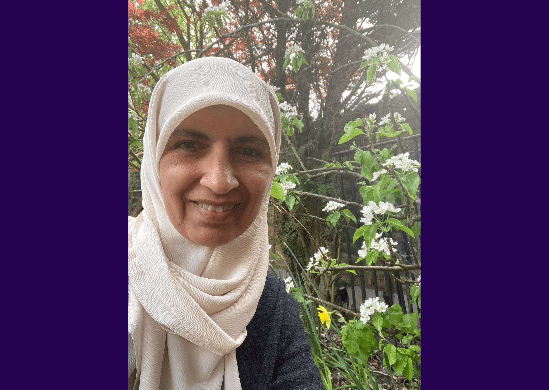 Image of living kidney donor Selma standing in front of a large flowering tree outside, smiling for the camera.