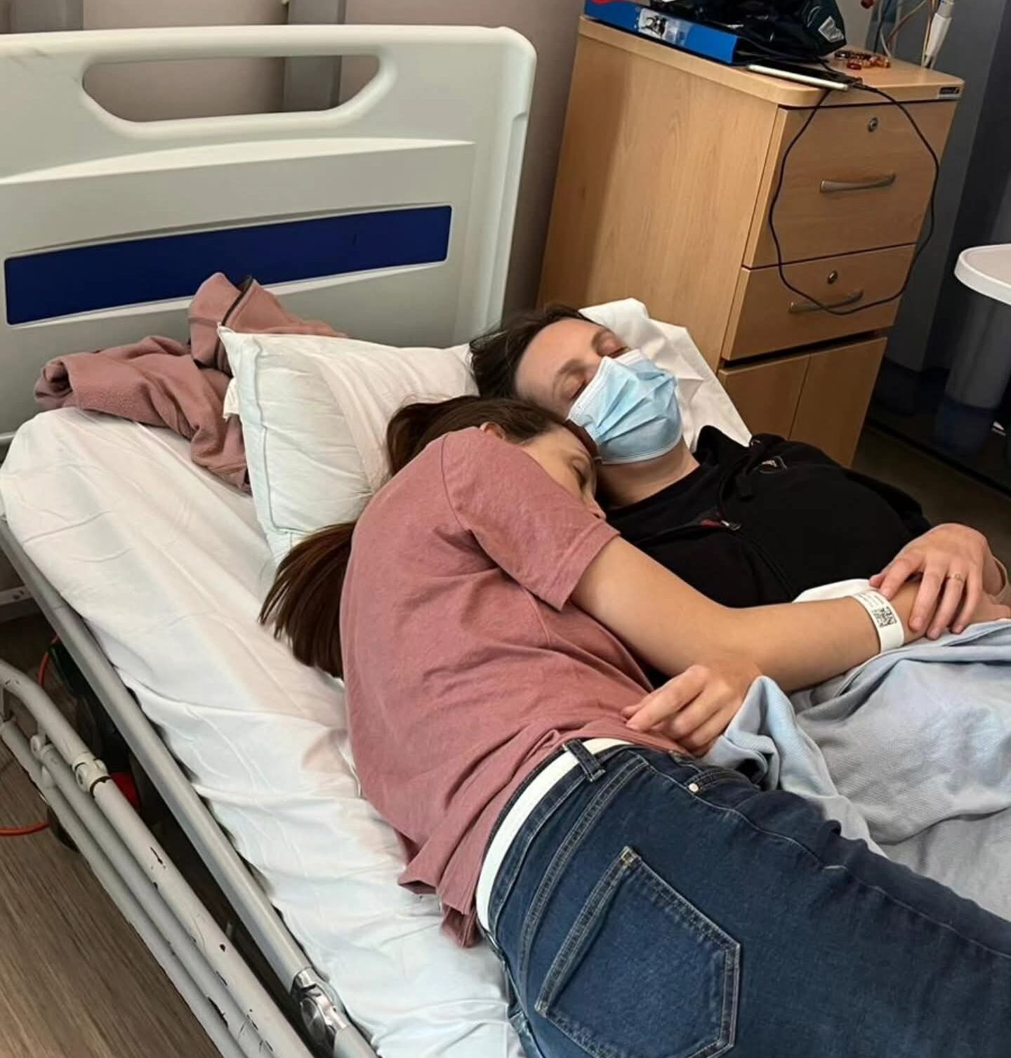 Living kidney donor Stacey and her twin sister laying asleep on a hospital bed together, cuddling one another while they sleep.