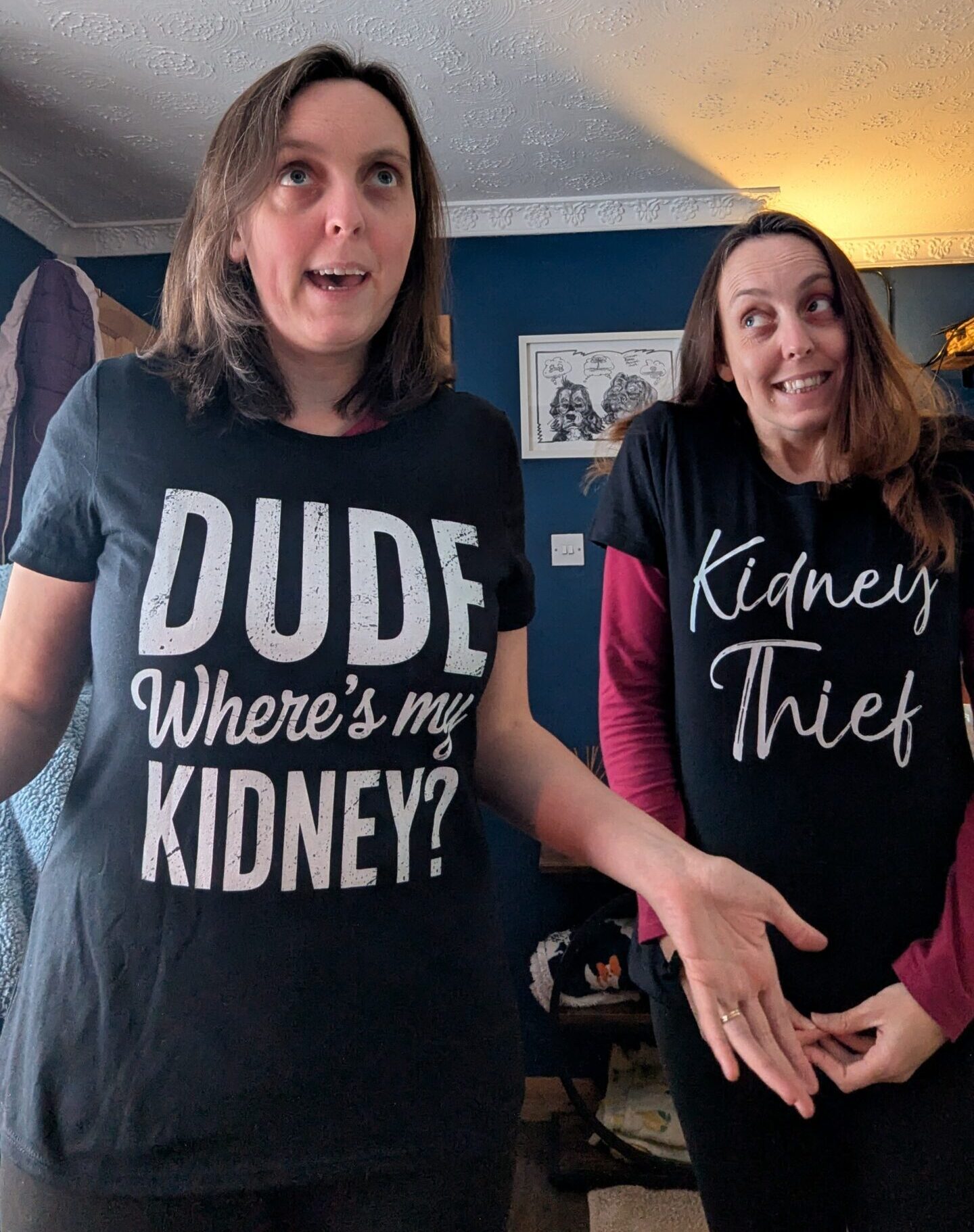 Living kidney donor Stacey alongside her twin and kidney recipient. Stacey is wearing a grey top featuring the words 'Dude, where's my kidney?' and shrugging with a smile, while her sister smiles sheepishly alongside her while wearing a grey top that says 'kidney thief'