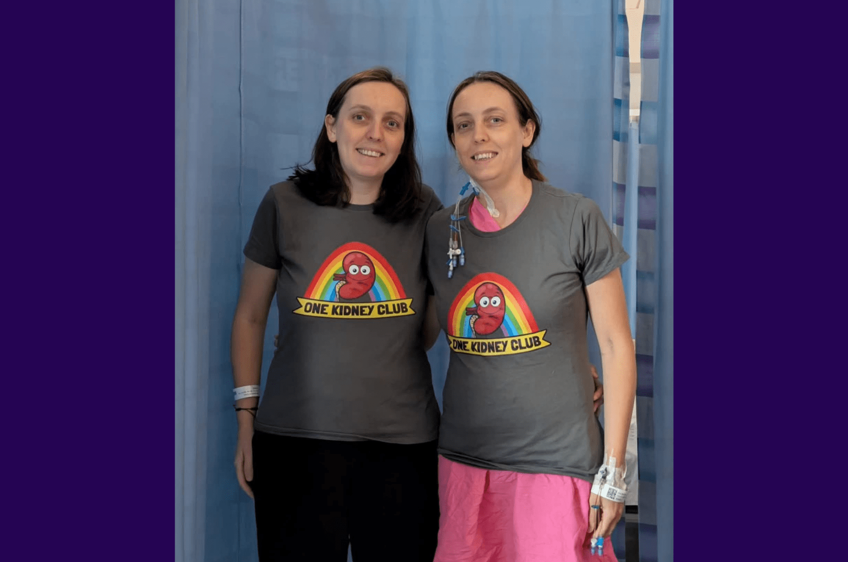 Living kidney donor Stacey alongside her twin sister and kidney recipient. They are standing in front of a blue hospital curtain and are both smiling for the camera, each wearing a grey top featuring a kidney of a cartoon kidney with eyes. Underneath the kidney are the words 'One kidney club'.