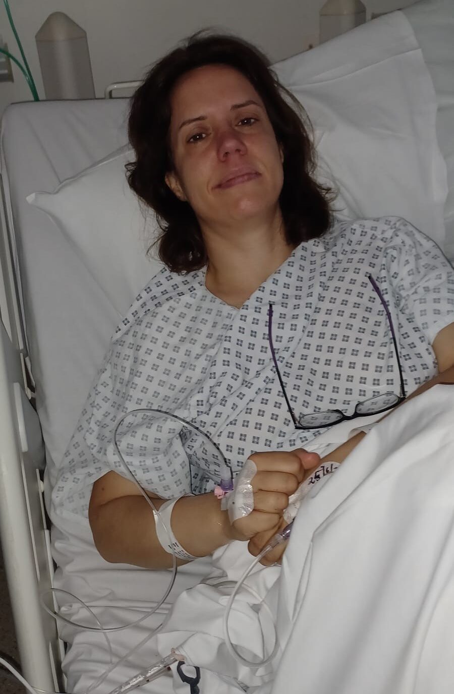 Living kidney donor Wilma in a hospital gown lying on a hospital bed, with her glasses resting on her stomach.